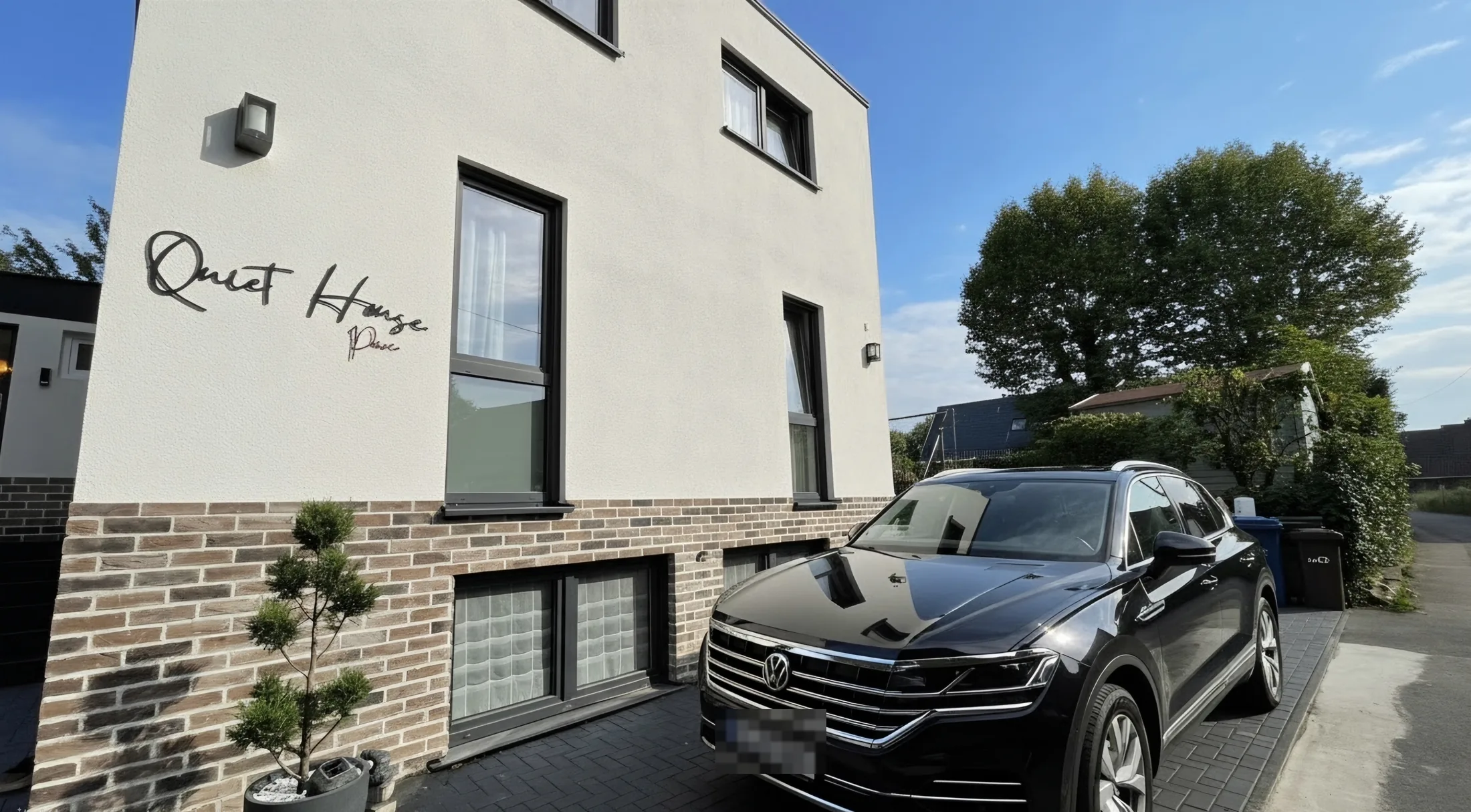 Quiet House Pure in Leverkusen-Steinbüchel: Hausansicht mit Schriftzug, Eingang und Privatparkplatz